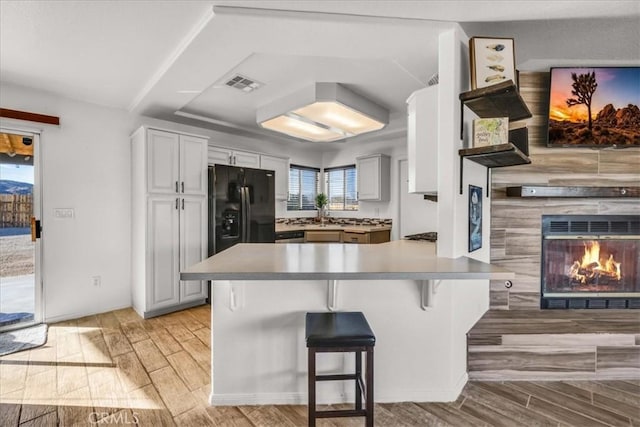 kitchen featuring visible vents, a kitchen breakfast bar, a peninsula, wood finish floors, and black fridge