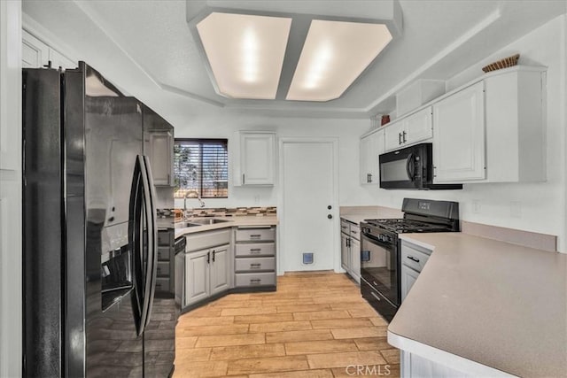 kitchen with white cabinets, light countertops, light wood-type flooring, black appliances, and a sink