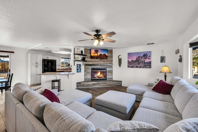 tiled living room with ceiling fan, a textured ceiling, and a tiled fireplace