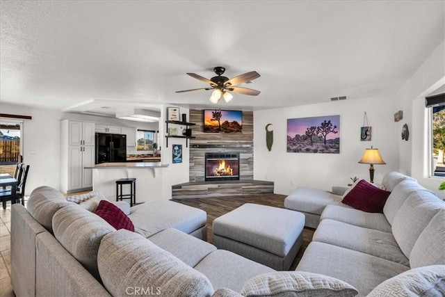 living room featuring ceiling fan, visible vents, and a tiled fireplace