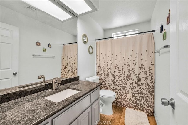 full bath with toilet, a shower with shower curtain, wood finished floors, vanity, and visible vents