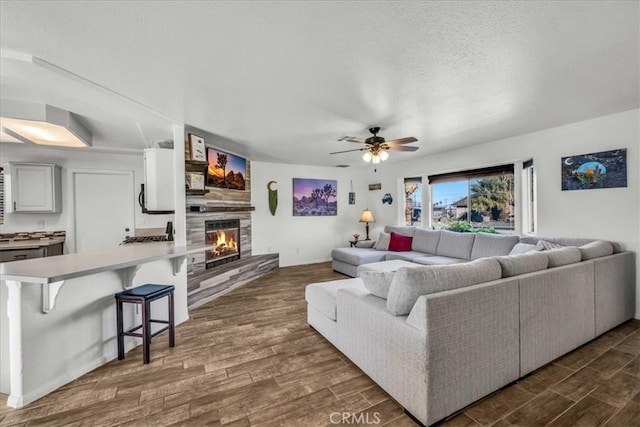 living room featuring a textured ceiling, ceiling fan, and a large fireplace