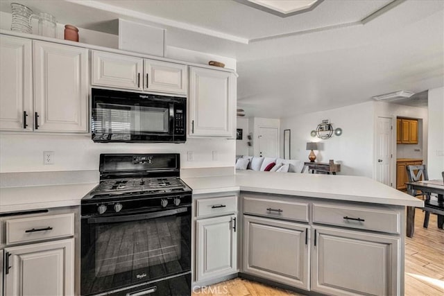 kitchen featuring light wood finished floors, light countertops, open floor plan, a peninsula, and black appliances