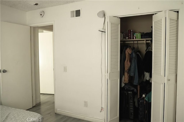 bedroom with light hardwood / wood-style floors, a textured ceiling, and a closet