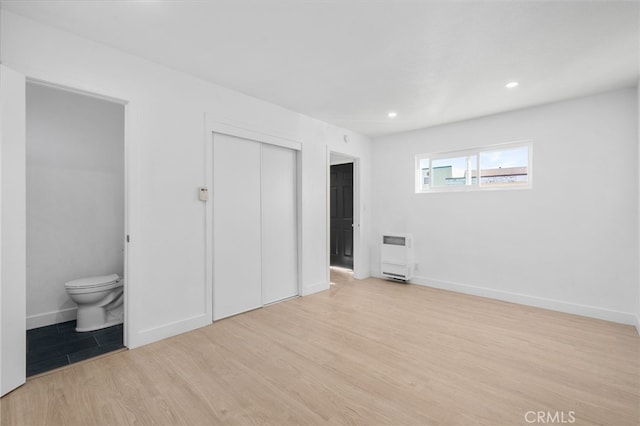 unfurnished bedroom with ensuite bathroom, heating unit, a closet, and light hardwood / wood-style flooring