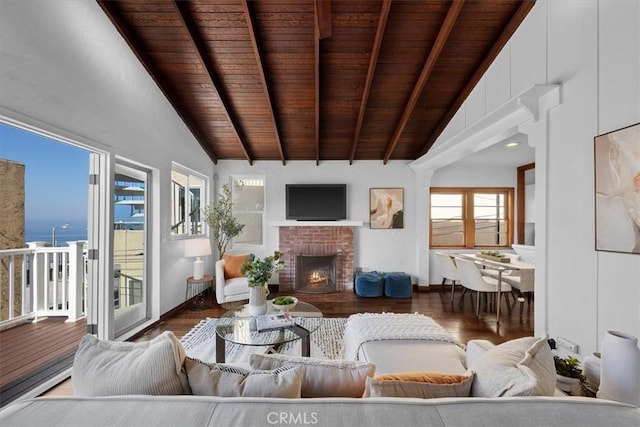 living room with vaulted ceiling with beams, dark wood-type flooring, a brick fireplace, and a water view