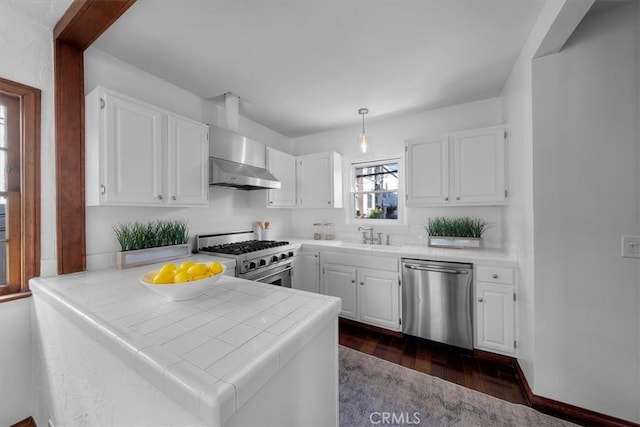 kitchen featuring appliances with stainless steel finishes, white cabinets, tile countertops, kitchen peninsula, and wall chimney exhaust hood