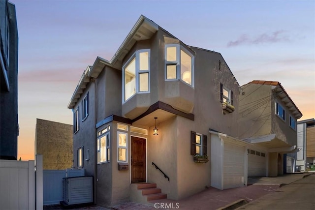 contemporary house featuring a garage, entry steps, fence, and stucco siding