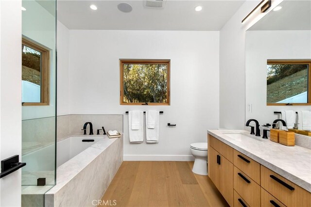 bathroom with a relaxing tiled tub, vanity, toilet, and hardwood / wood-style flooring