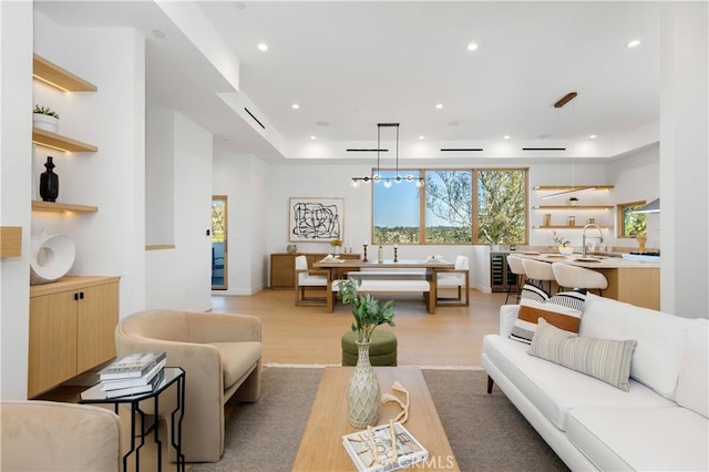 living room with beverage cooler, sink, a raised ceiling, and light hardwood / wood-style floors