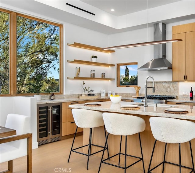 2456 Loy Ln, Los Angeles, CA 90041 - kitchen with wall chimney range hood, light stone counters, a breakfast bar area, beverage cooler, and modern cabinets