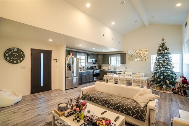 living room with vaulted ceiling with beams, sink, and light wood-type flooring