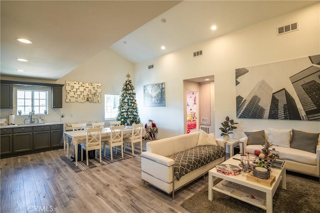 living room with high vaulted ceiling, sink, and light hardwood / wood-style floors