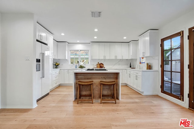 kitchen featuring high end refrigerator, light wood-type flooring, a kitchen breakfast bar, a kitchen island, and white cabinets