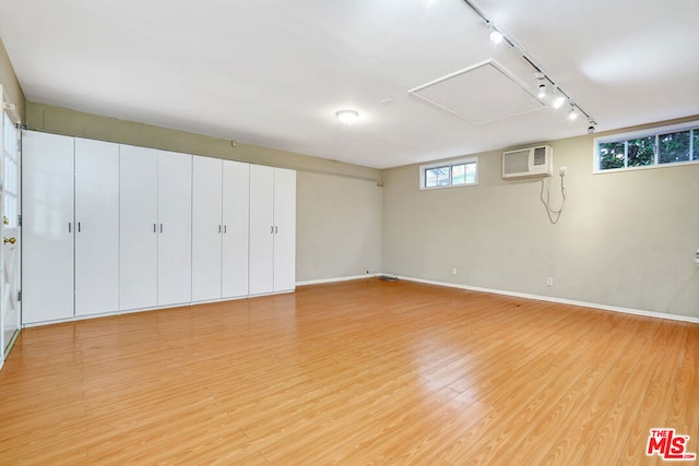 basement featuring rail lighting, a wall mounted AC, and light hardwood / wood-style flooring