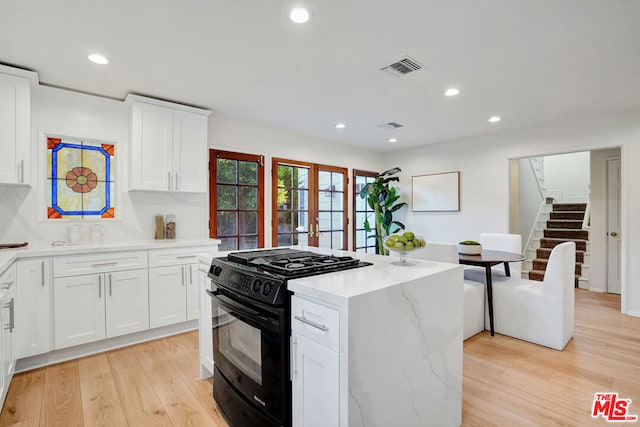 kitchen featuring black gas range oven, light stone countertops, light hardwood / wood-style floors, and white cabinets