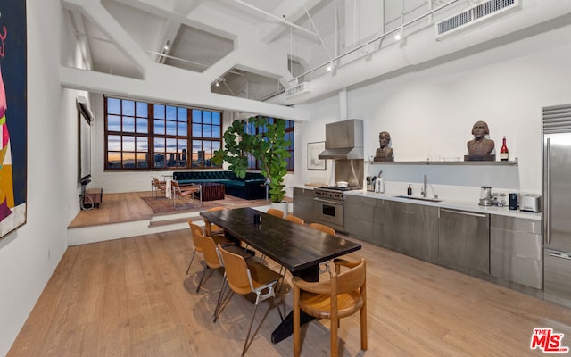 kitchen with wall chimney exhaust hood, sink, stainless steel stove, a towering ceiling, and light hardwood / wood-style floors