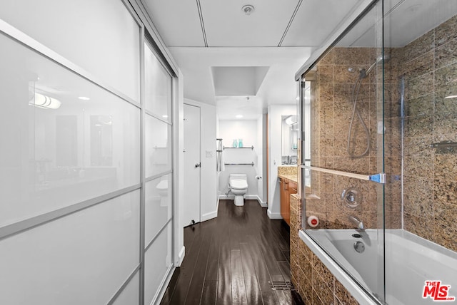 full bathroom featuring wood-type flooring, bath / shower combo with glass door, toilet, and vanity