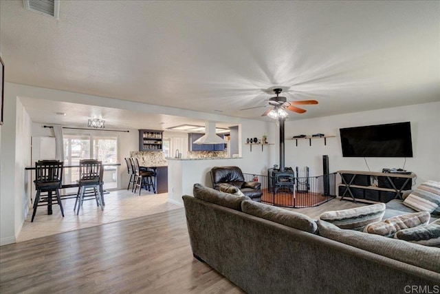 living room with light wood-type flooring, a wood stove, and ceiling fan