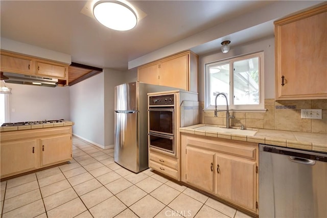 kitchen with sink, backsplash, stainless steel appliances, light brown cabinetry, and tile countertops