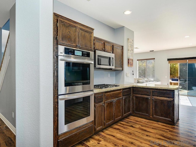 kitchen with dark brown cabinets, kitchen peninsula, appliances with stainless steel finishes, and dark wood-type flooring