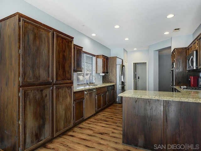 kitchen with sink, light hardwood / wood-style flooring, kitchen peninsula, stainless steel appliances, and light stone counters