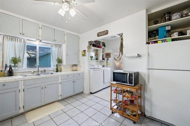 kitchen featuring washing machine and clothes dryer, sink, light tile patterned floors, white refrigerator, and tile counters