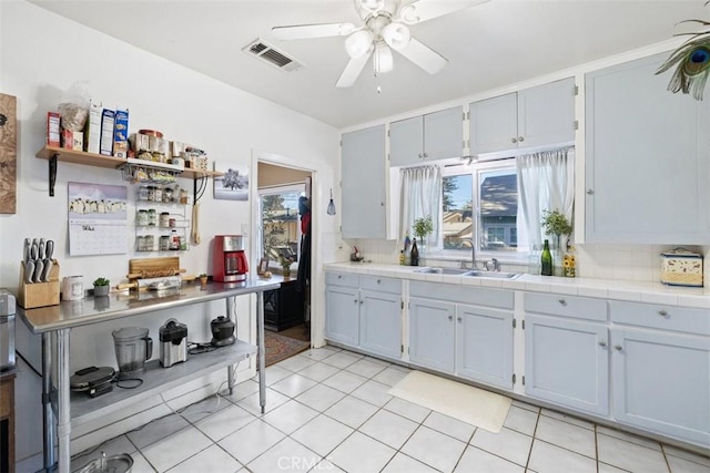 kitchen with sink, tasteful backsplash, light tile patterned floors, tile counters, and ceiling fan