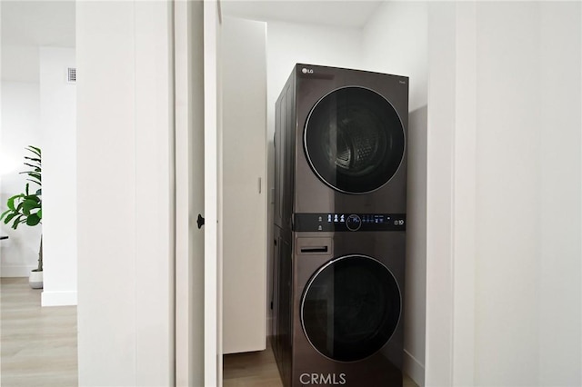 laundry area with stacked washer / dryer and light hardwood / wood-style flooring