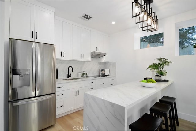 kitchen featuring light stone countertops, stainless steel fridge with ice dispenser, white cabinetry, sink, and pendant lighting