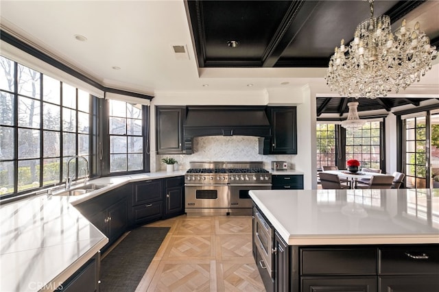 kitchen with decorative light fixtures, sink, range with two ovens, wall chimney range hood, and an inviting chandelier