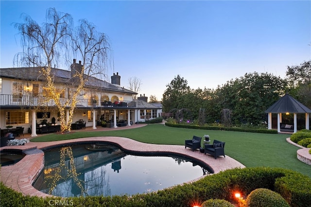 pool at dusk with a gazebo, a yard, and a patio area