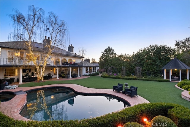 pool at dusk with a patio area, a yard, and a gazebo