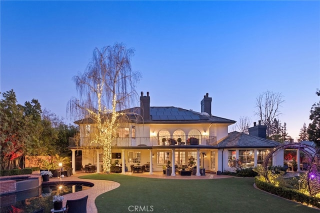 back house at dusk featuring a balcony, a yard, and a patio area