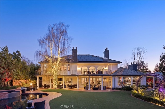 back house at dusk with a yard, a patio area, and a balcony