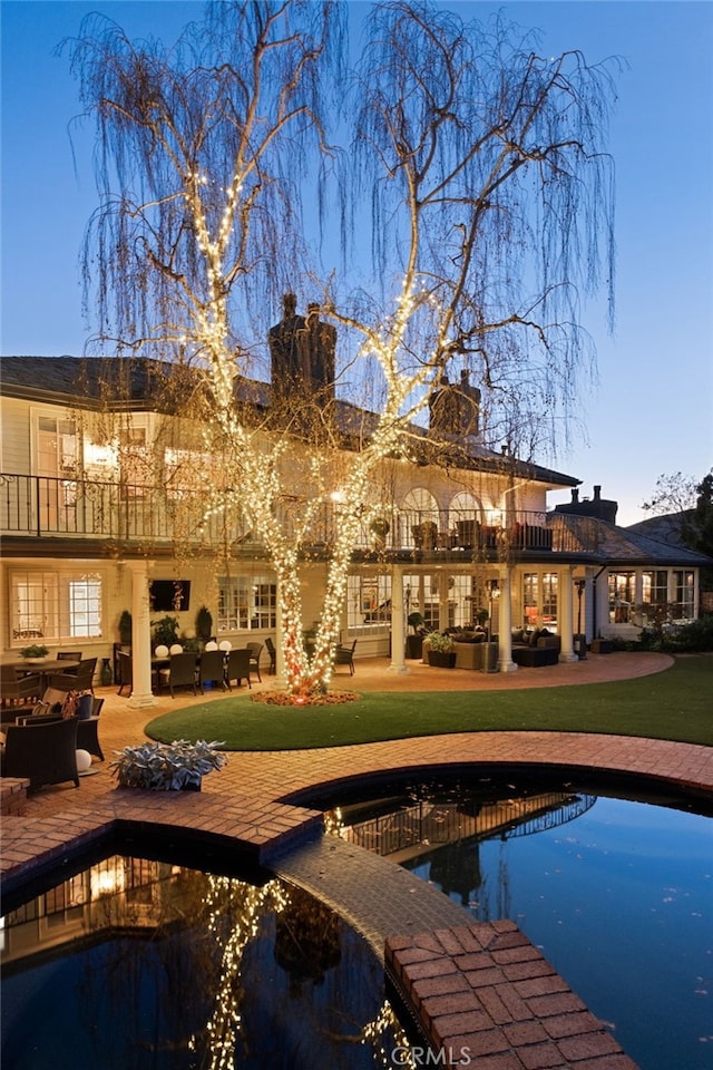 back house at dusk featuring a balcony, a yard, and a patio area