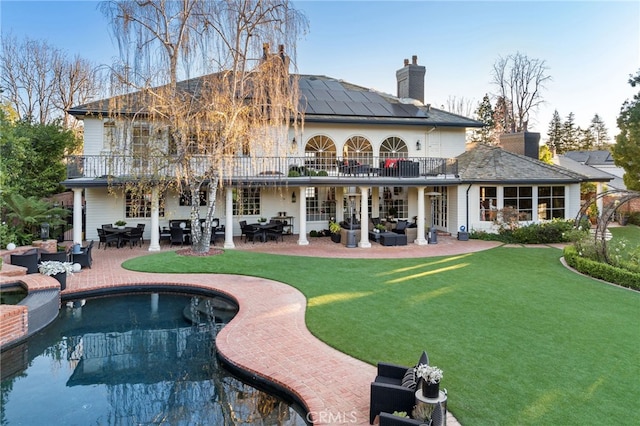 rear view of property with a yard, outdoor lounge area, a patio area, solar panels, and a balcony