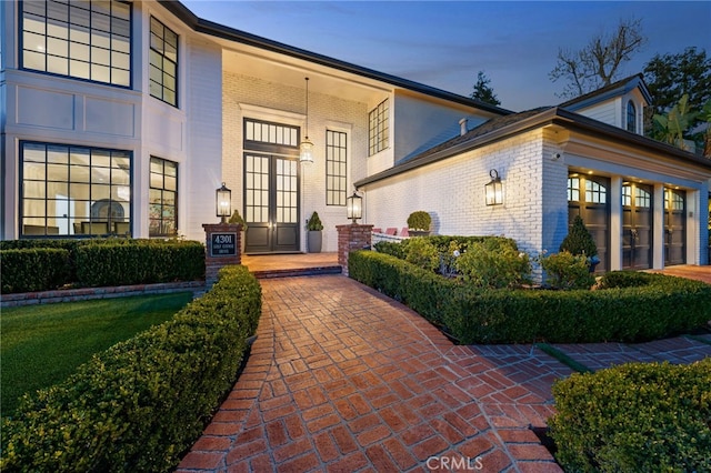 exterior entry at dusk featuring french doors, brick siding, and a garage