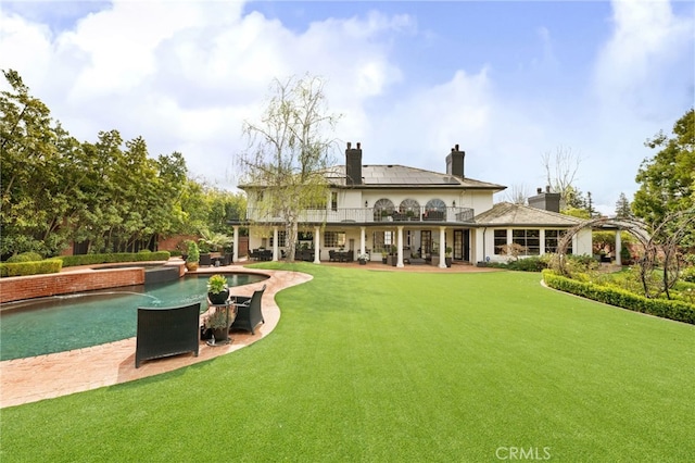 rear view of property with a pool with connected hot tub, a lawn, a chimney, a balcony, and a patio area