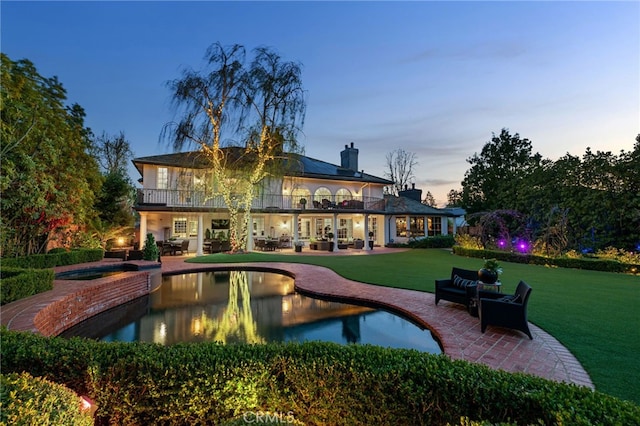 back of house at dusk with a patio area, a yard, a chimney, and a balcony