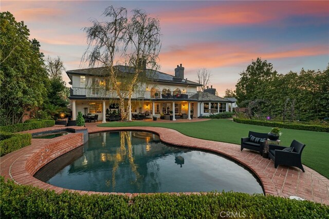 back of property at dusk with an outdoor living space, a patio, a balcony, and a lawn