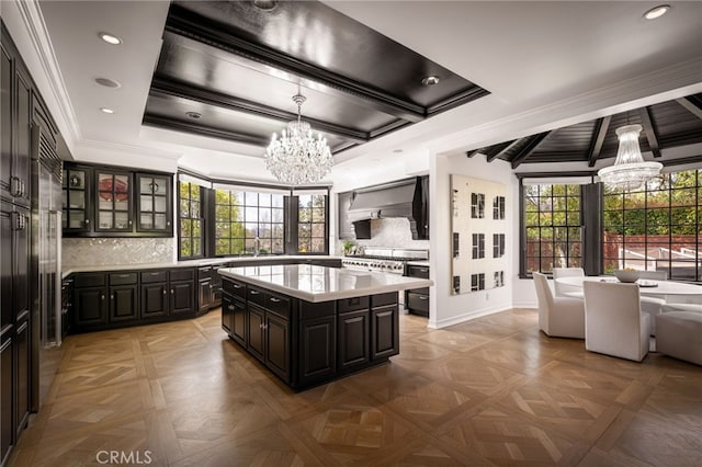 kitchen featuring a kitchen island, premium range hood, light countertops, ornamental molding, and an inviting chandelier