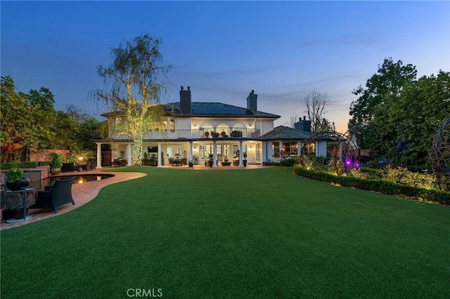 rear view of property featuring a balcony, a chimney, a lawn, and a patio area