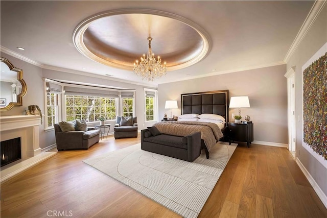 bedroom featuring a tray ceiling, wood finished floors, a lit fireplace, baseboards, and a chandelier