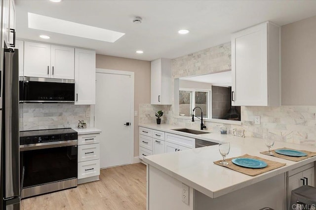 kitchen with a sink, stainless steel appliances, light countertops, and white cabinetry