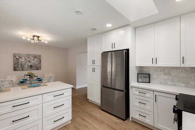 kitchen featuring decorative backsplash, freestanding refrigerator, light countertops, light wood-style floors, and white cabinetry