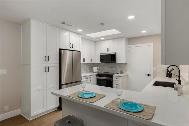 kitchen featuring visible vents, a peninsula, stainless steel appliances, light countertops, and a sink