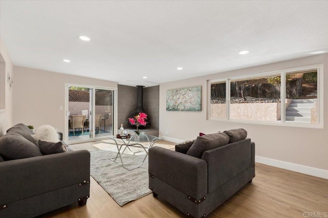 living room featuring a wood stove, light wood-type flooring, baseboards, and recessed lighting