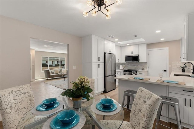 kitchen with stainless steel appliances, a breakfast bar, a sink, white cabinets, and light countertops