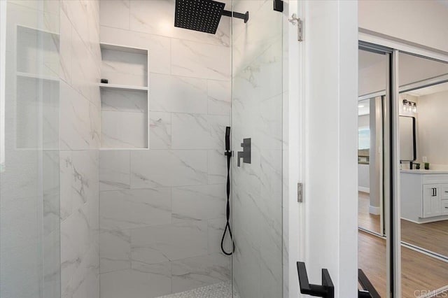 full bathroom with vanity, a marble finish shower, and wood finished floors